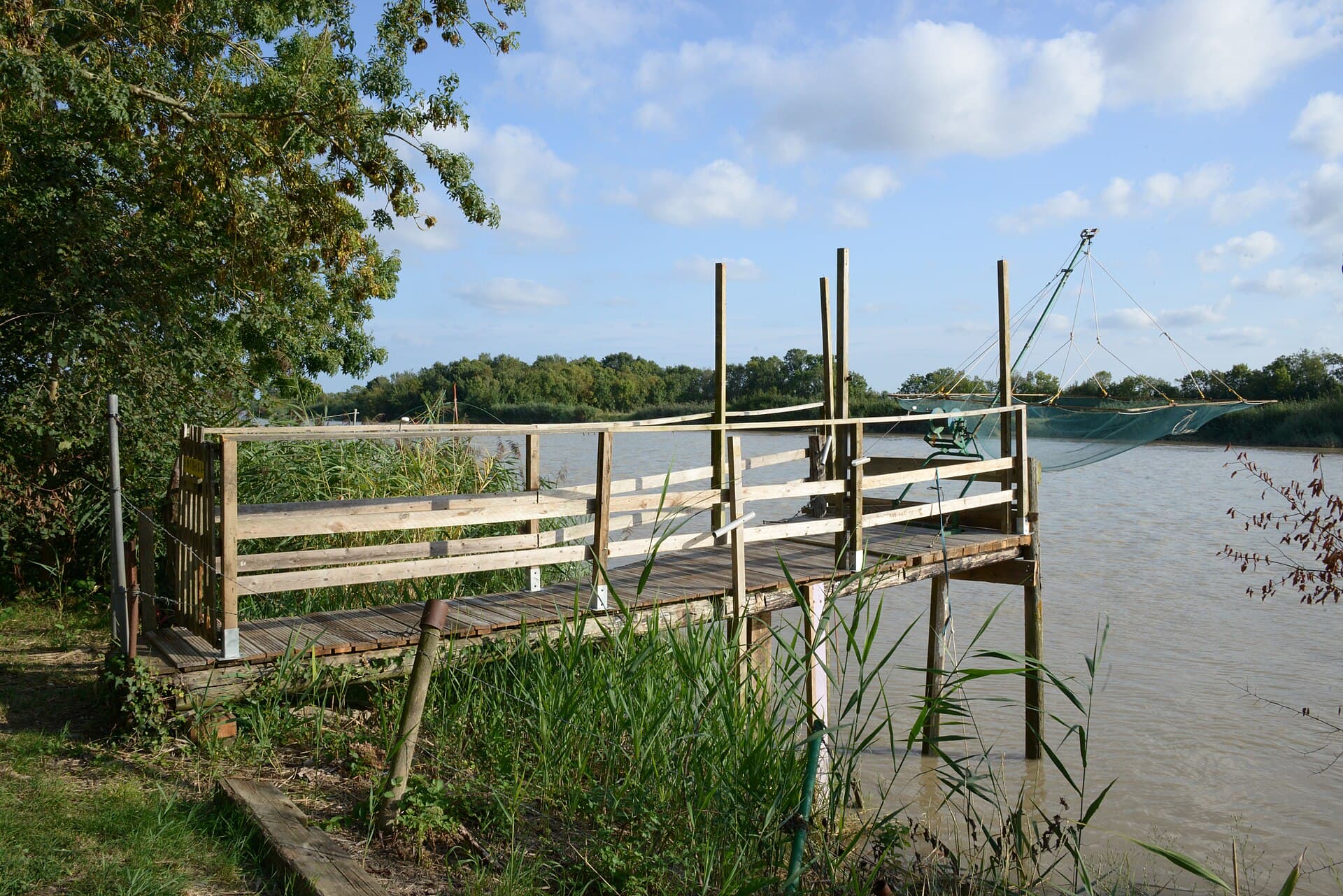 Ponton de pêche au carrelet sur pilotis de bois, filet suspendu au-dessus de la Charente, sous un ciel bleu parsemé de nuages