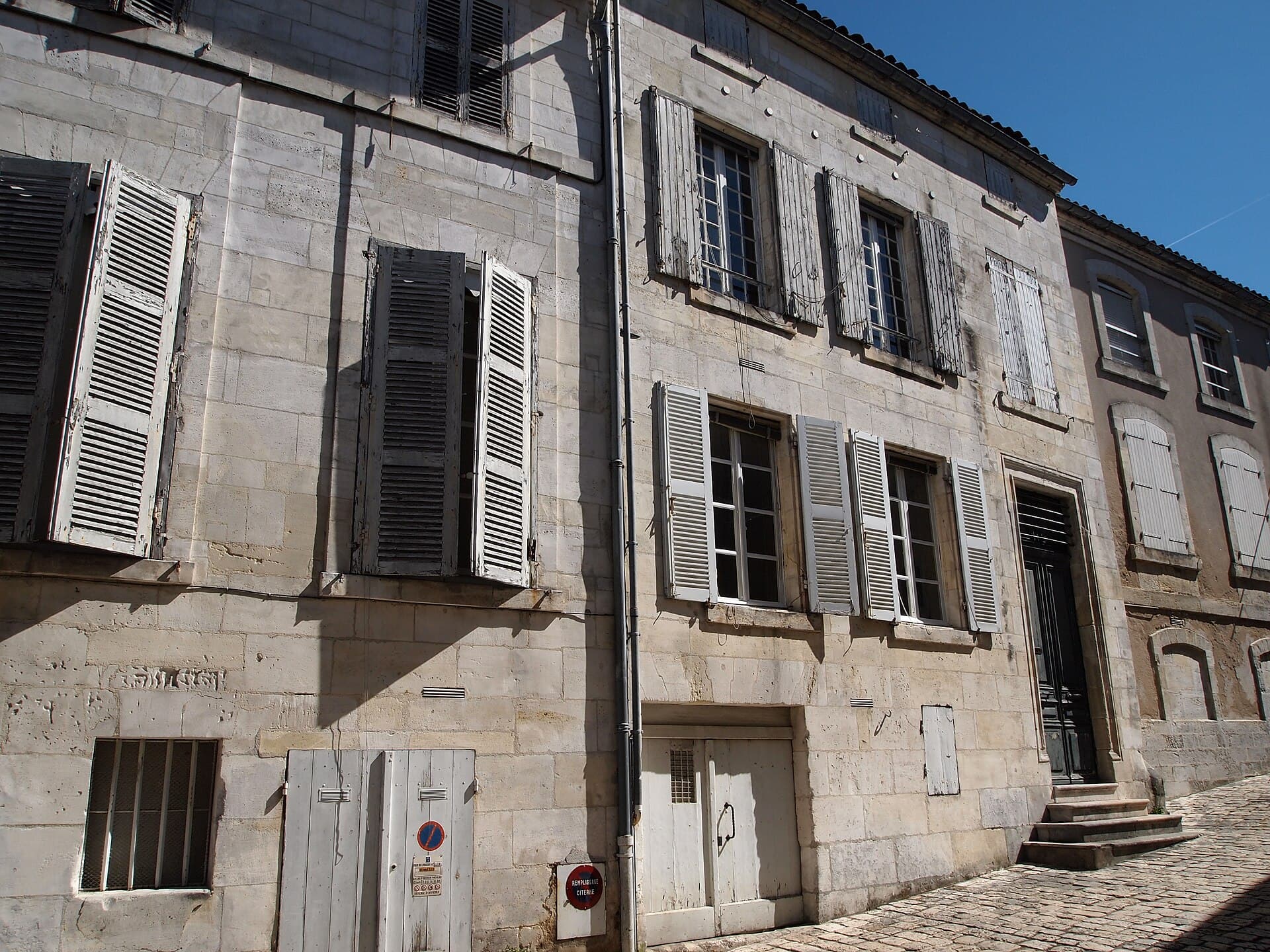 Façades en pierre de taille aux volets de bois d'une rue ancienne de Cognac, sous un ciel bleu d'été.