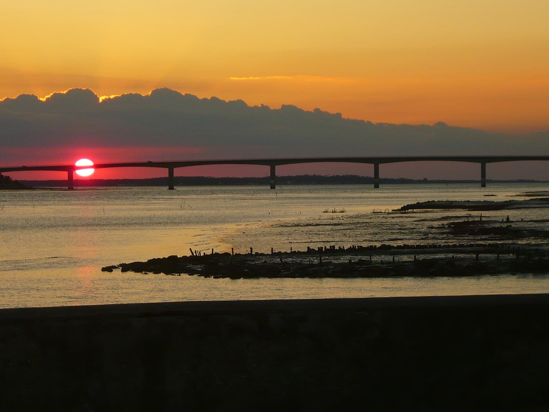 Le soleil descend derrière le viaduc d'Oléron, la mer et les estrans prennent des reflets orangés