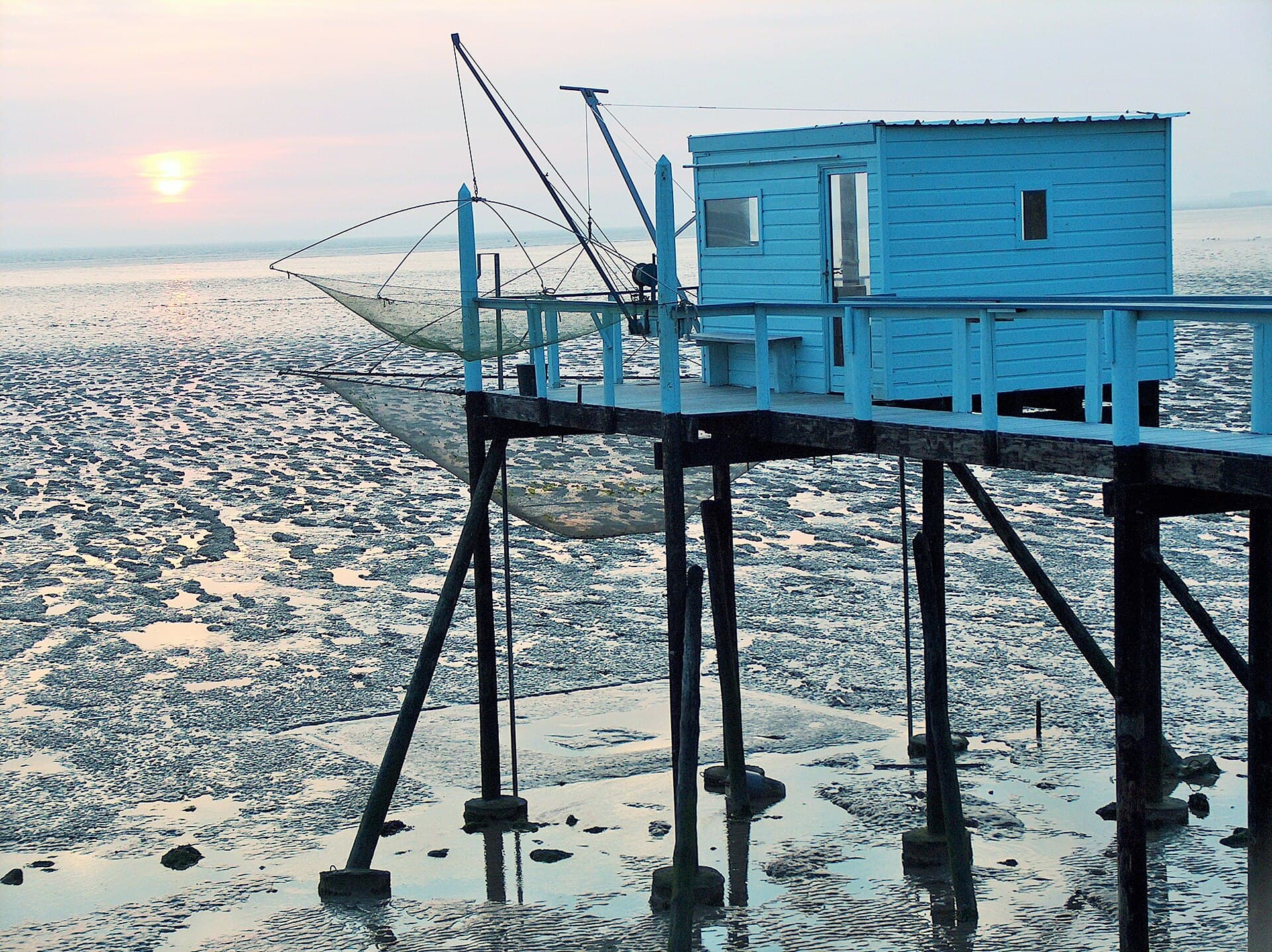Cabane de pêche à carrelet bleue sur pilotis, son filet relevé au-dessus de l'estran, au coucher du soleil à Fouras.