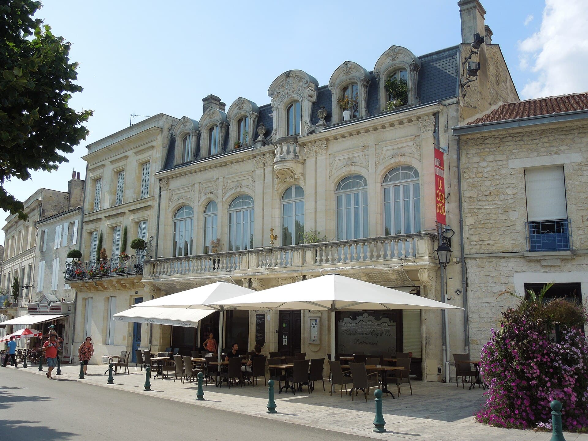 Façades anciennes en pierre claire aux lucarnes ouvragées et terrasse ombragée sur la place du Château, à Jonzac