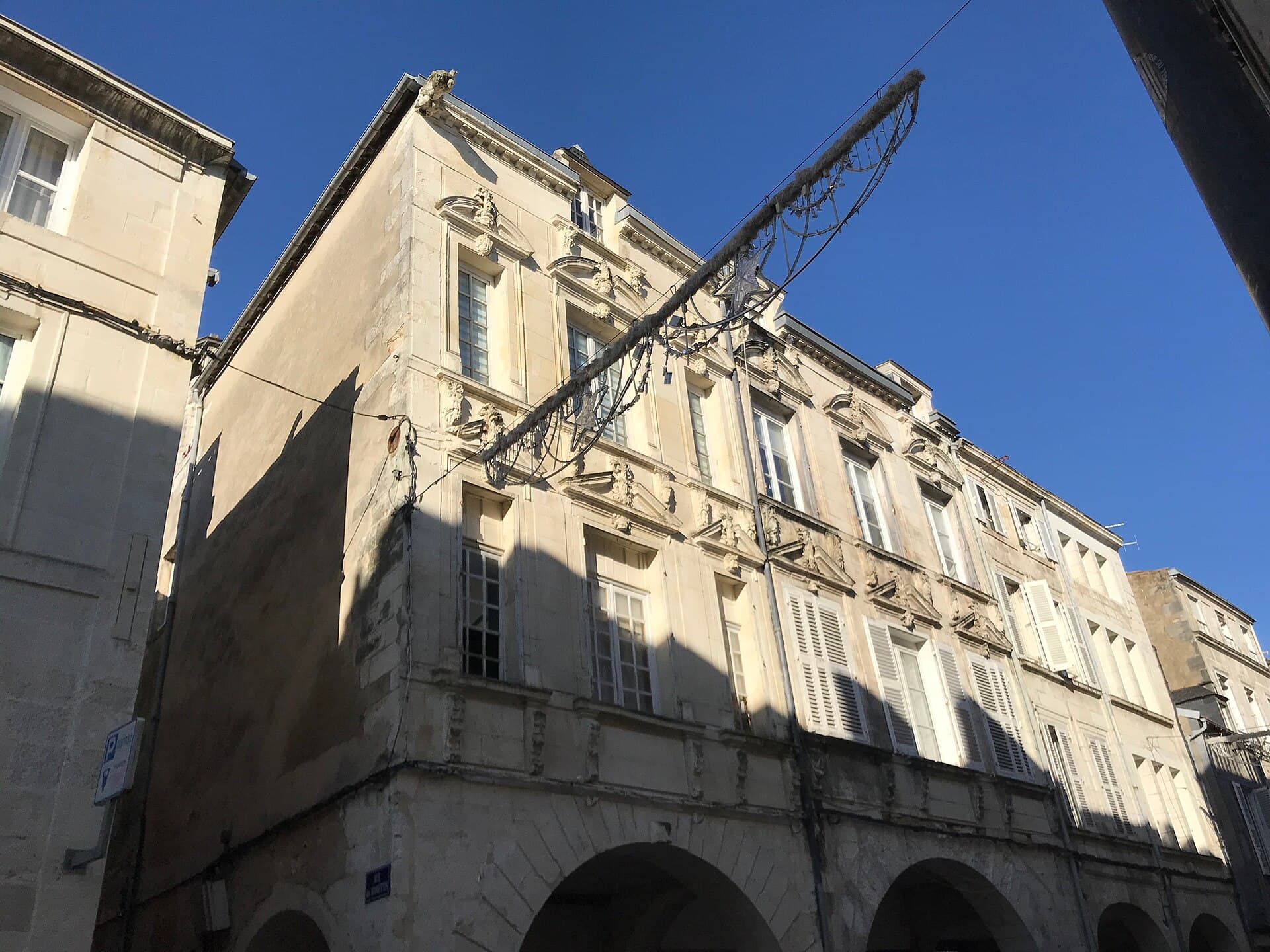 Façade ancienne en pierre de taille de la rue des Merciers à La Rochelle, avec ses arcades au rez-de-chaussée, sous un ciel bleu.