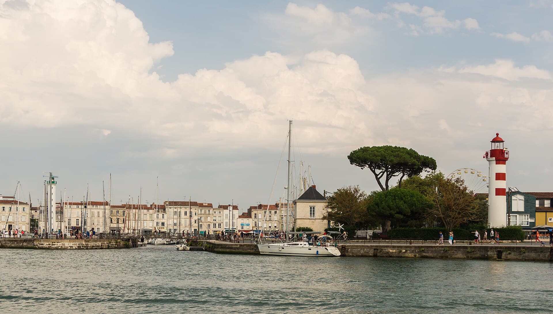 Le port de La Rochelle vu depuis l'eau, avec son feu rouge et blanc, un voilier amarré et les façades claires des quais.