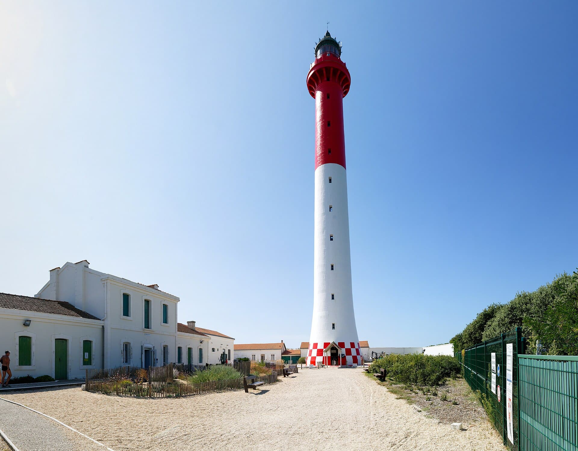 Le phare rouge et blanc de la Coubre dominant les maisons blanches à volets verts des gardiens, sous un ciel d'été dégagé