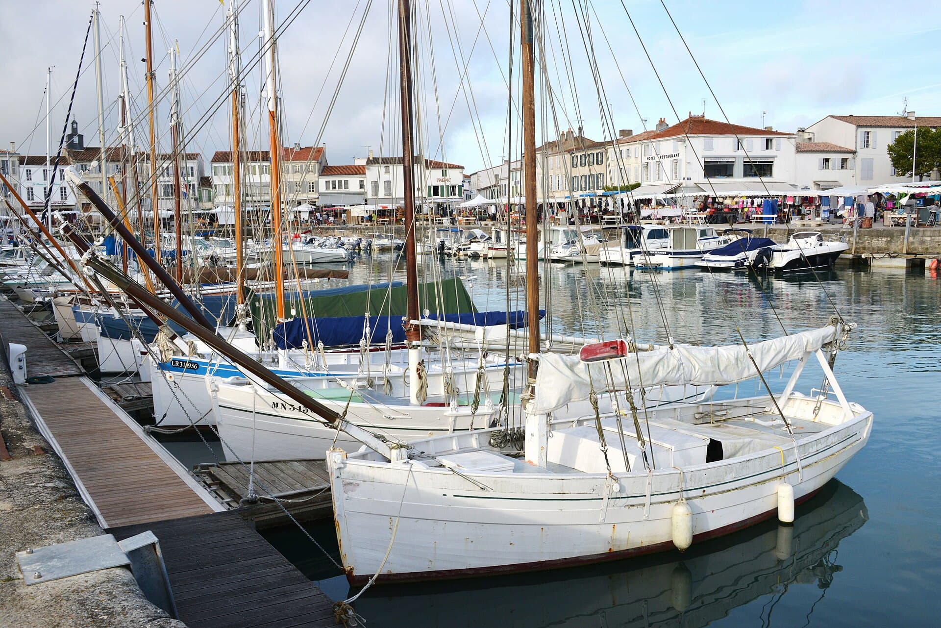 Vieux gréements aux coques blanches amarrés dans le port de La Flotte, devant le marché et les maisons blanches du quai