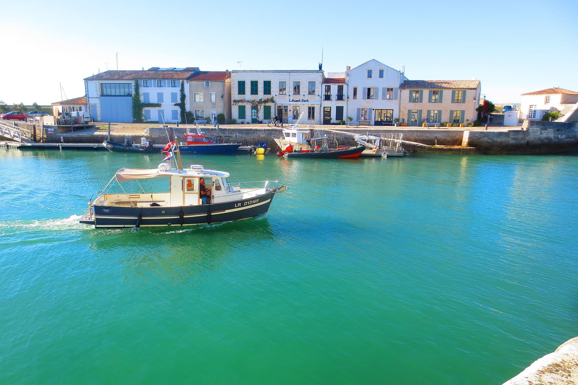 Le port de Saint-Martin-de-Ré, un bateau de pêche traversant l'eau turquoise devant un alignement de maisons blanches à volets clairs