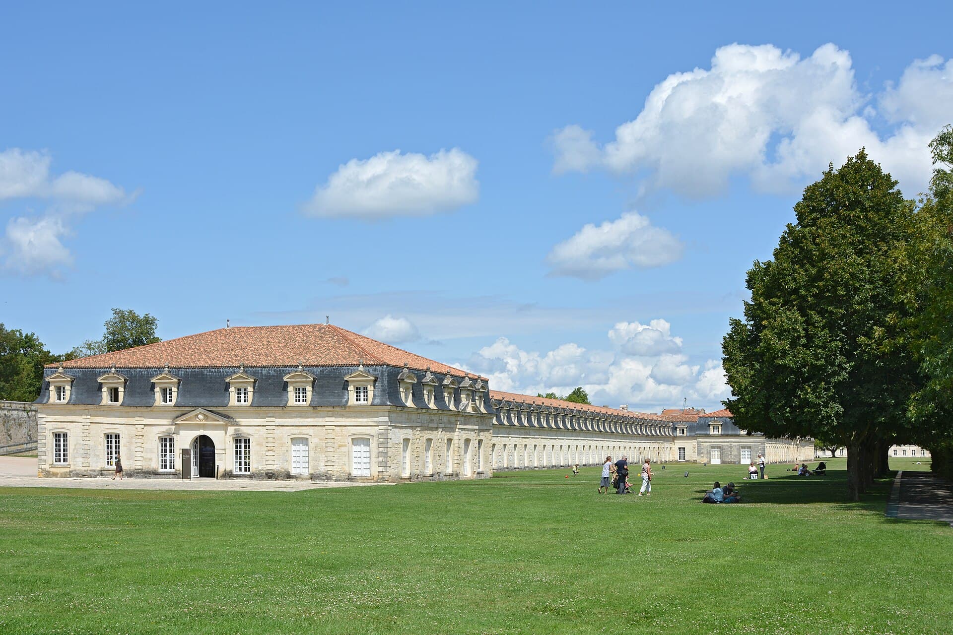 La Corderie Royale de Rochefort, longue façade de pierre claire coiffée de tuiles, bordée d'une vaste pelouse sous un ciel d'été.
