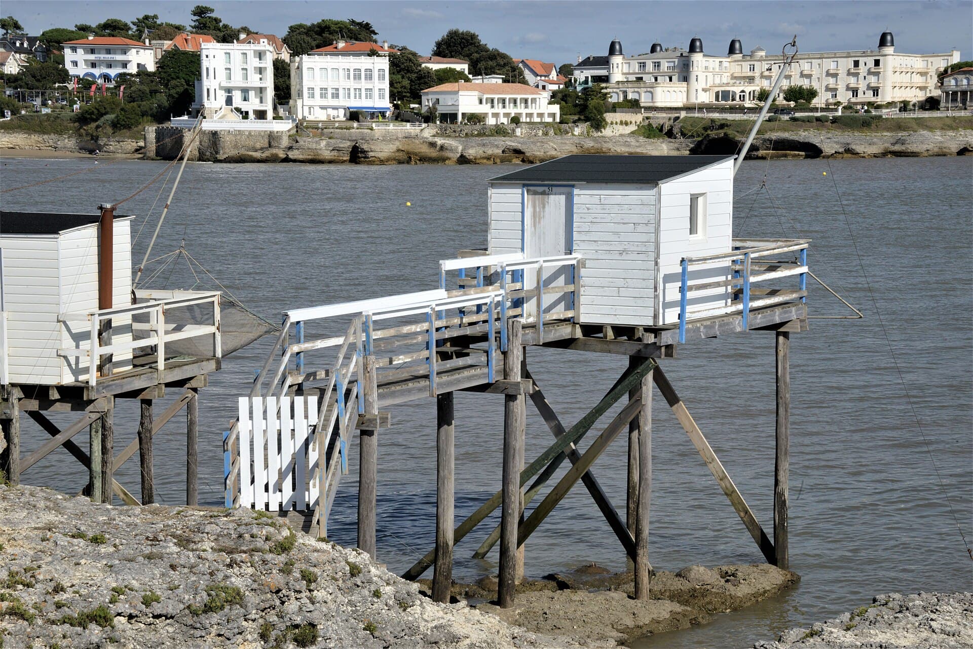 Cabanes de pêche au carrelet blanches sur pilotis au bord de la conche de Pontaillac, face aux villas balnéaires et aux hôtels du front de mer