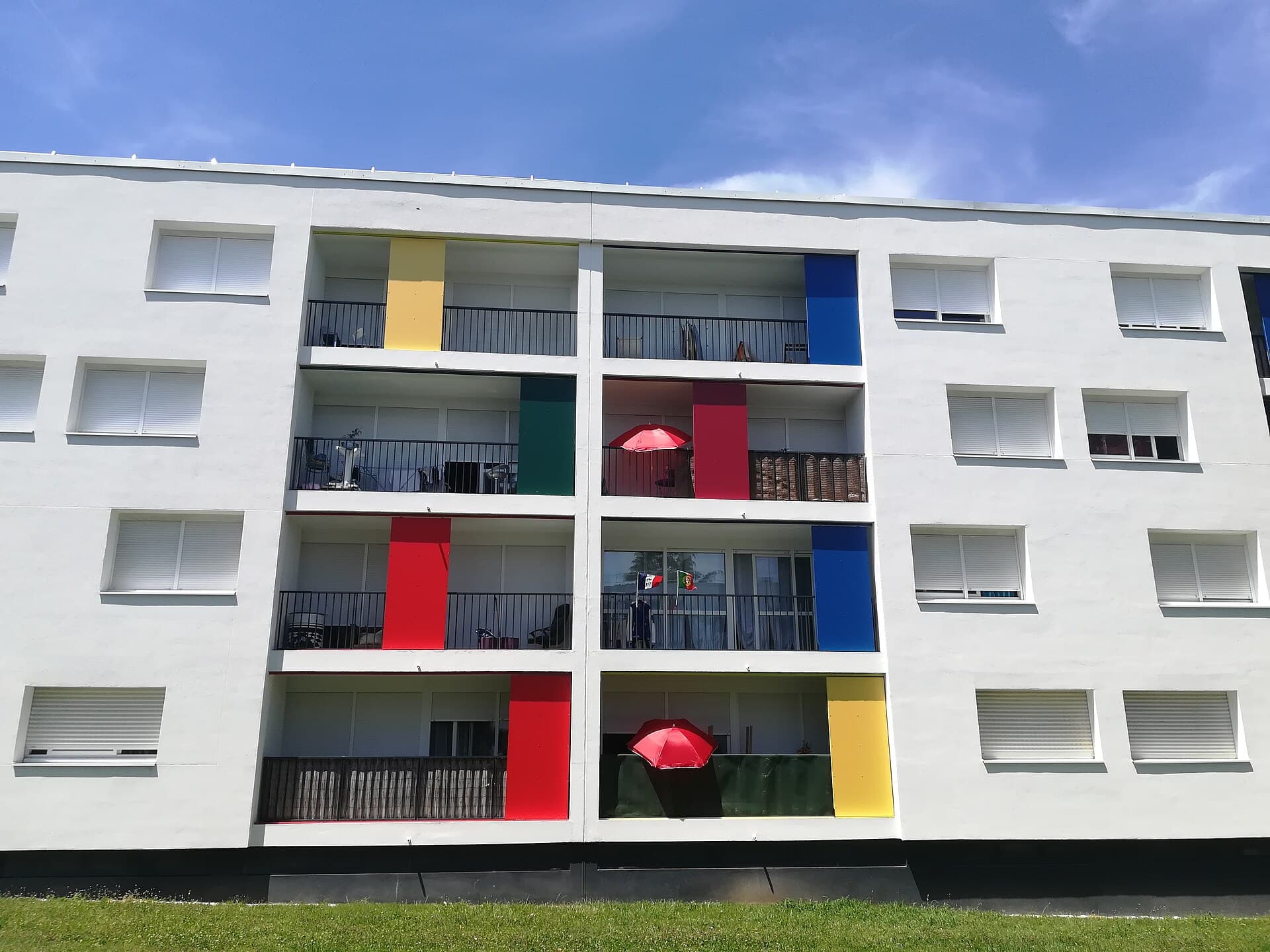 Façade blanche d'un immeuble de logements rénové à Royan, avec des balcons habités et des panneaux de couleurs vives jaune, bleu, vert et rouge