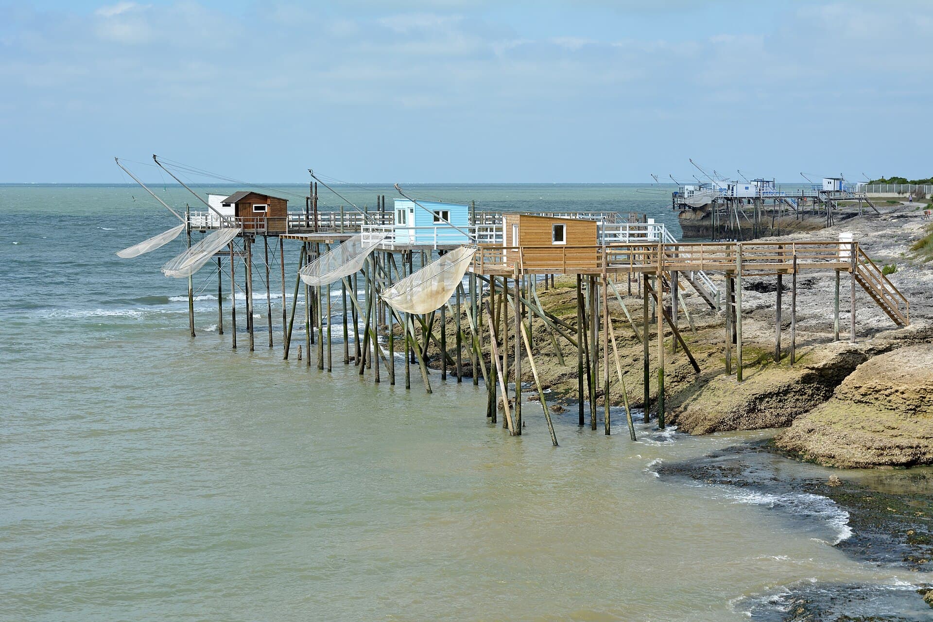 Une file de carrelets sur pilotis, filets de pêche déployés au-dessus de l'eau, le long du littoral de Saint-Palais-sur-Mer.