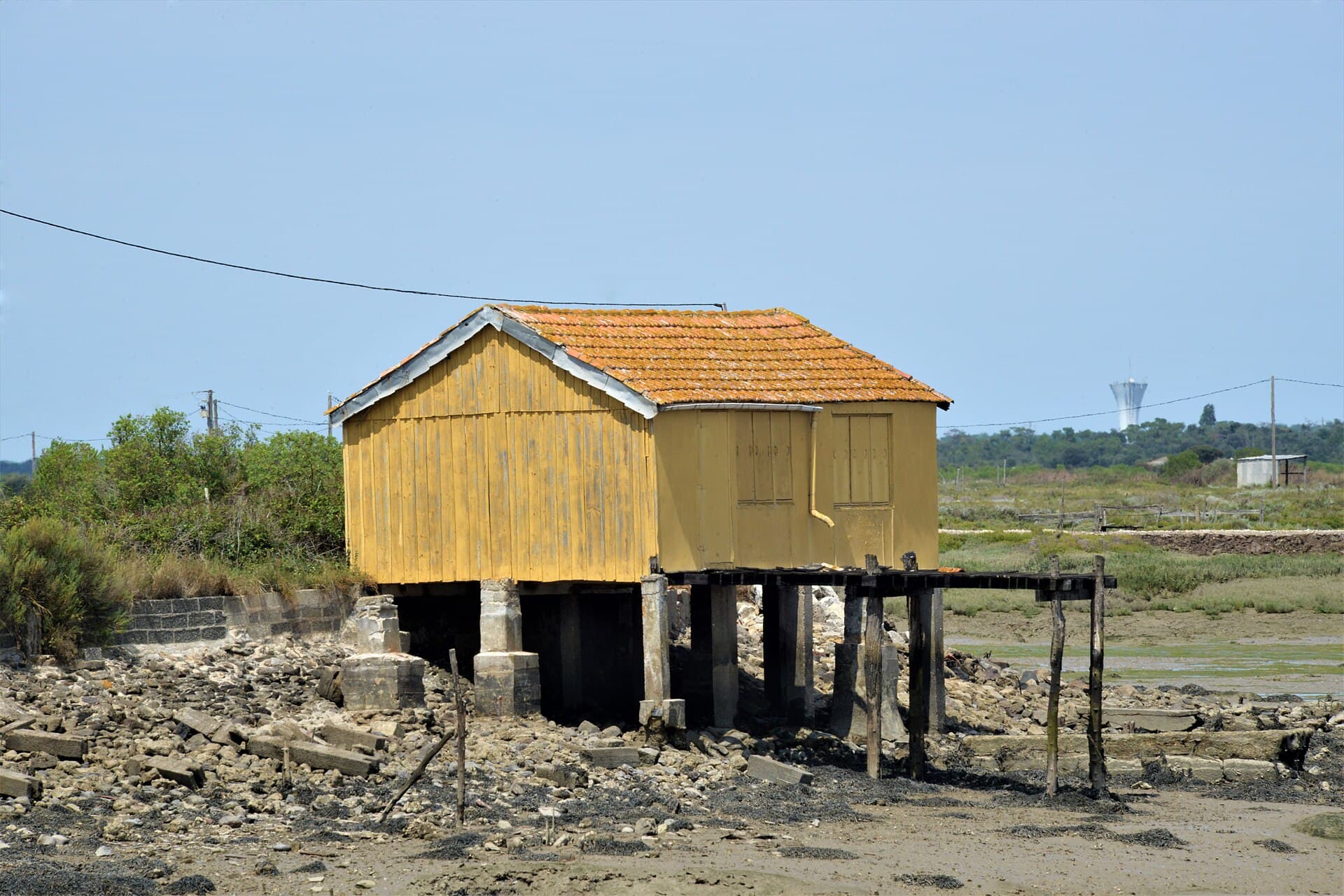 Une cabane en bois jaune à toit de tuiles, posée sur pilotis au bord du marais de Saint-Trojan-les-Bains, à marée basse