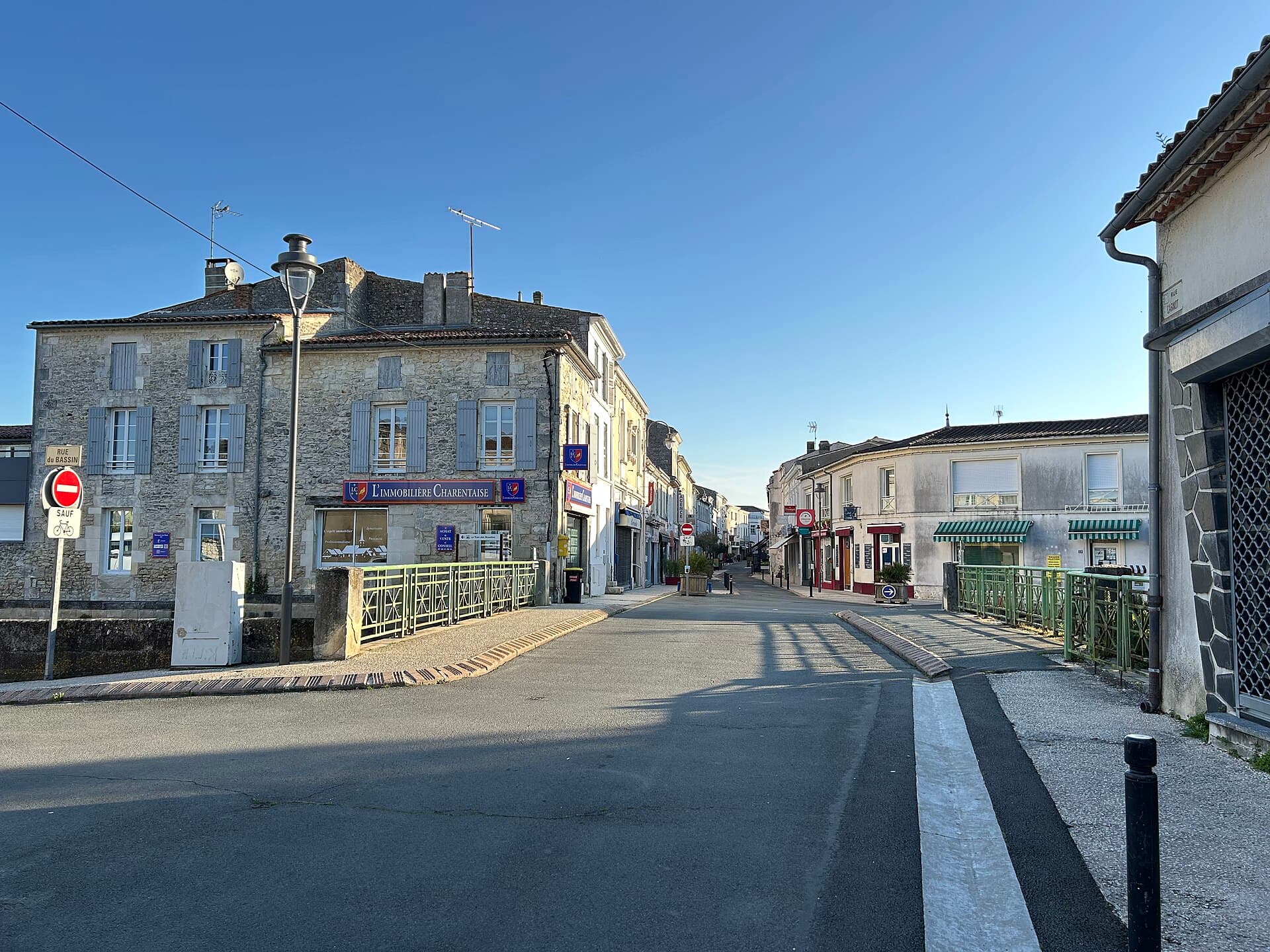 Maisons anciennes en pierre aux volets clairs bordant la rue au niveau du pont Carnot, à Saujon, sous un ciel bleu
