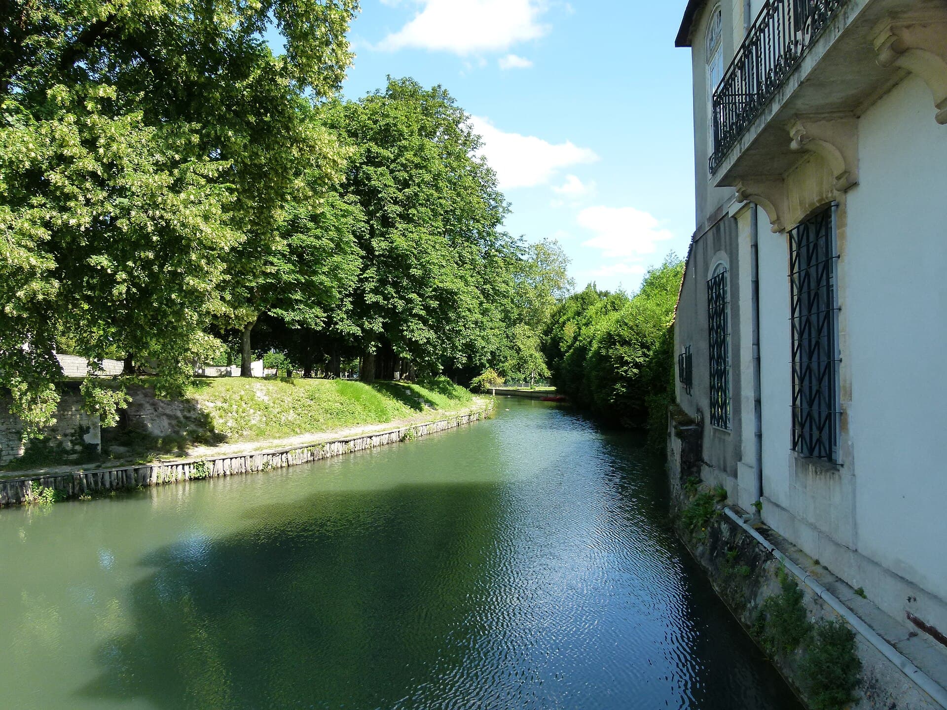 La rivière Gères bordée d'arbres et d'une façade ancienne à balcon en fer forgé, à Surgères